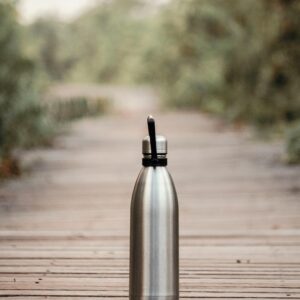 A stainless steel water bottle on a wooden path in an outdoor setting, surrounded by greenery.